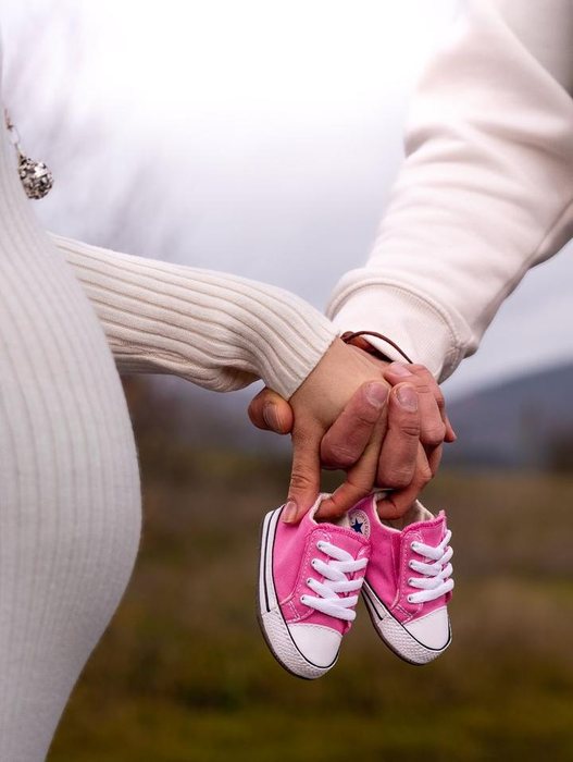 Pareja de la mano sosteniendo unas zapatillas de bebé rosas